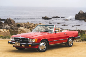 A red 1989 Mercedes 560SL convertible driving along a scenic coastal road provided for an entry into the letters from vintage Mercedes owners blog